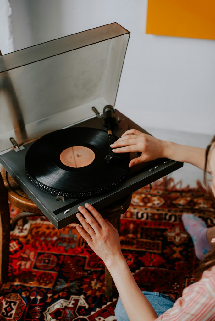 Photo of a person setting up a record on a record player in the corner of a room.